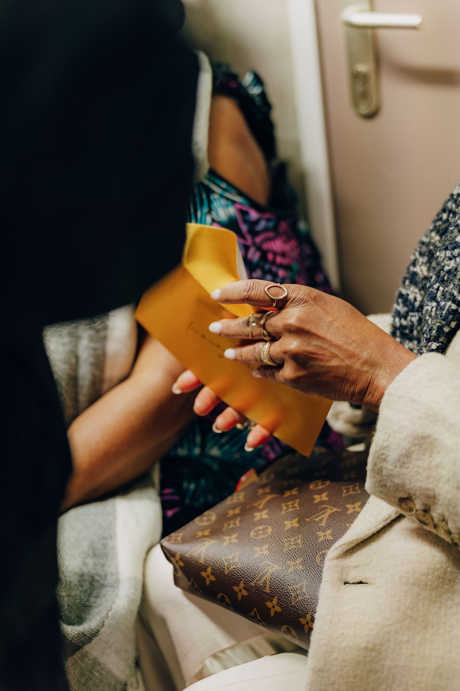 Hands holding a colored envelope with Louis Vuitton accessories visible in frame.