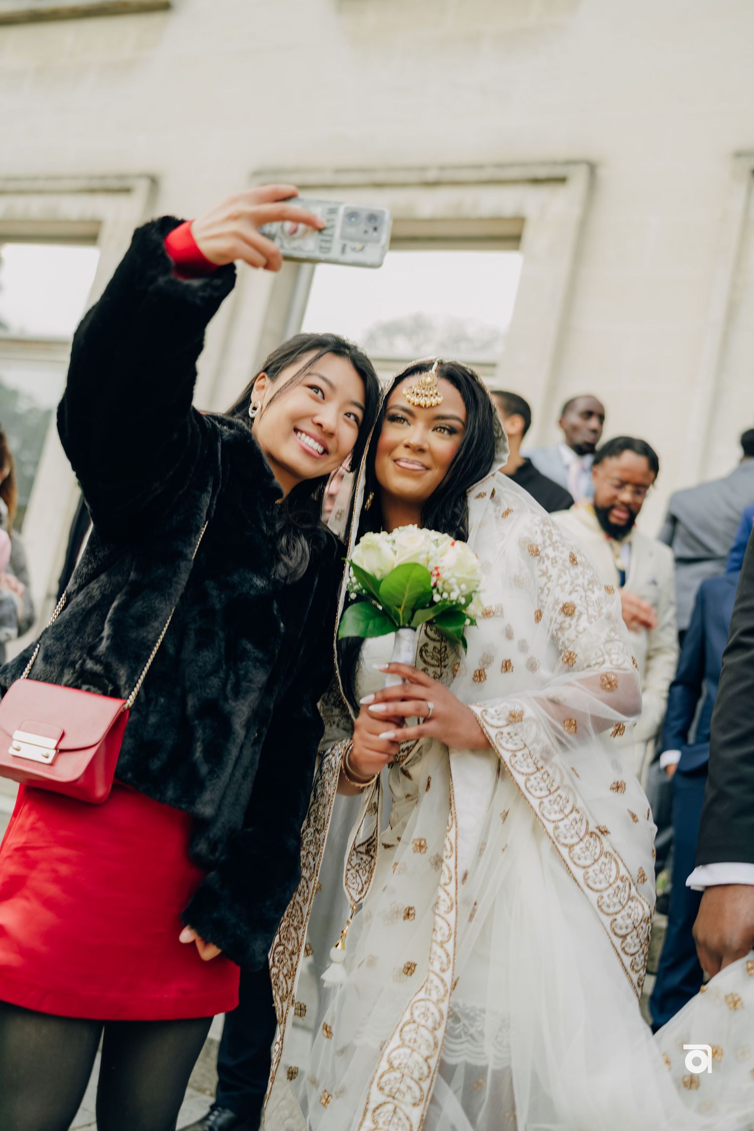 Wedding guests take selfies with the bride in her ornate traditional white and gold sari.