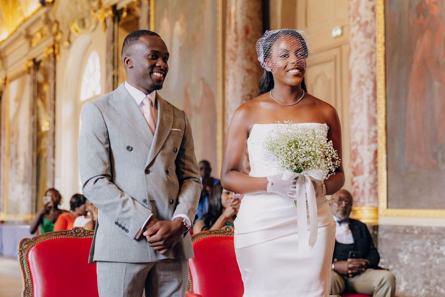 Wedding party in formal attire poses inside an ornate gold ballroom with elegant decor and architecture.