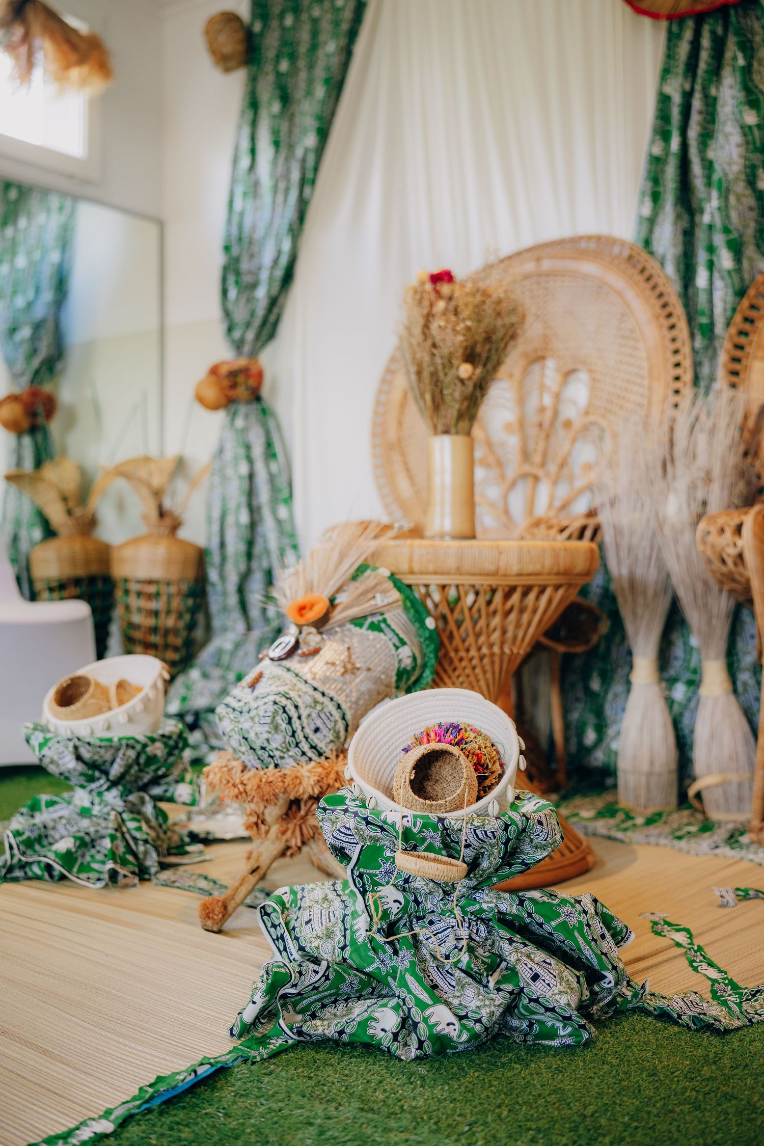 Decorative woven fans and tropical decor arranged on a table with green foliage and white curtains in the background.