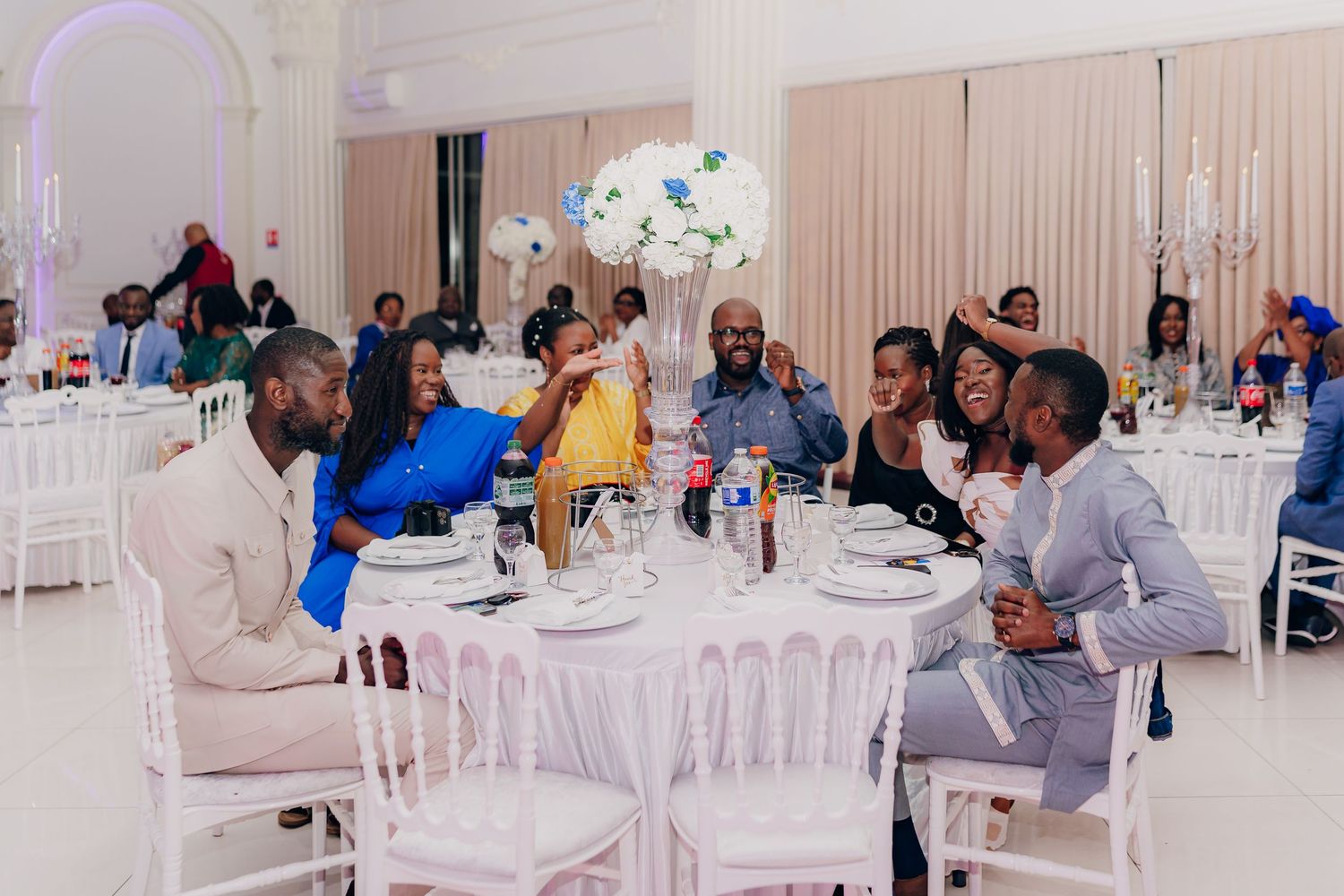 Wedding guests gather around an elegantly decorated table at a reception with white and blue decor.