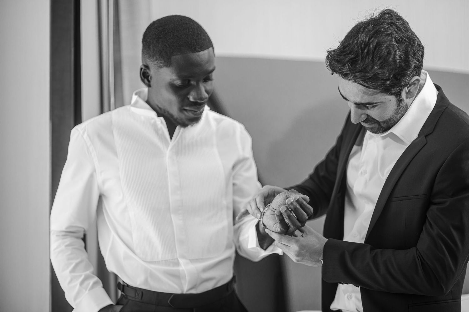 Black and white image of two people checking a timepiece during wedding preparations.