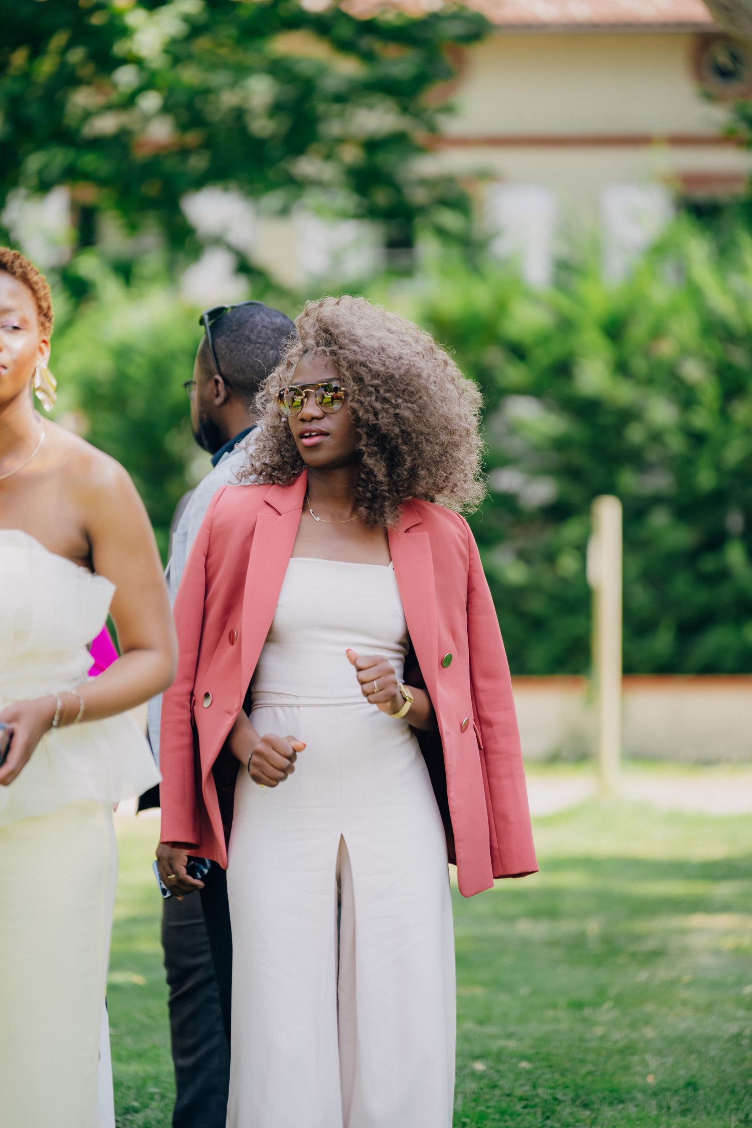 Guests mingle at an outdoor garden party wearing elegant pink and white attire.