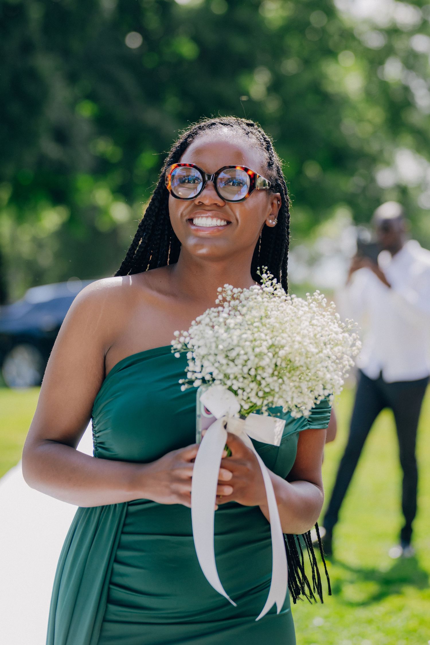 Bridesmaids in elegant dark green dresses hold delicate baby's breath bouquets at an outdoor ceremony.