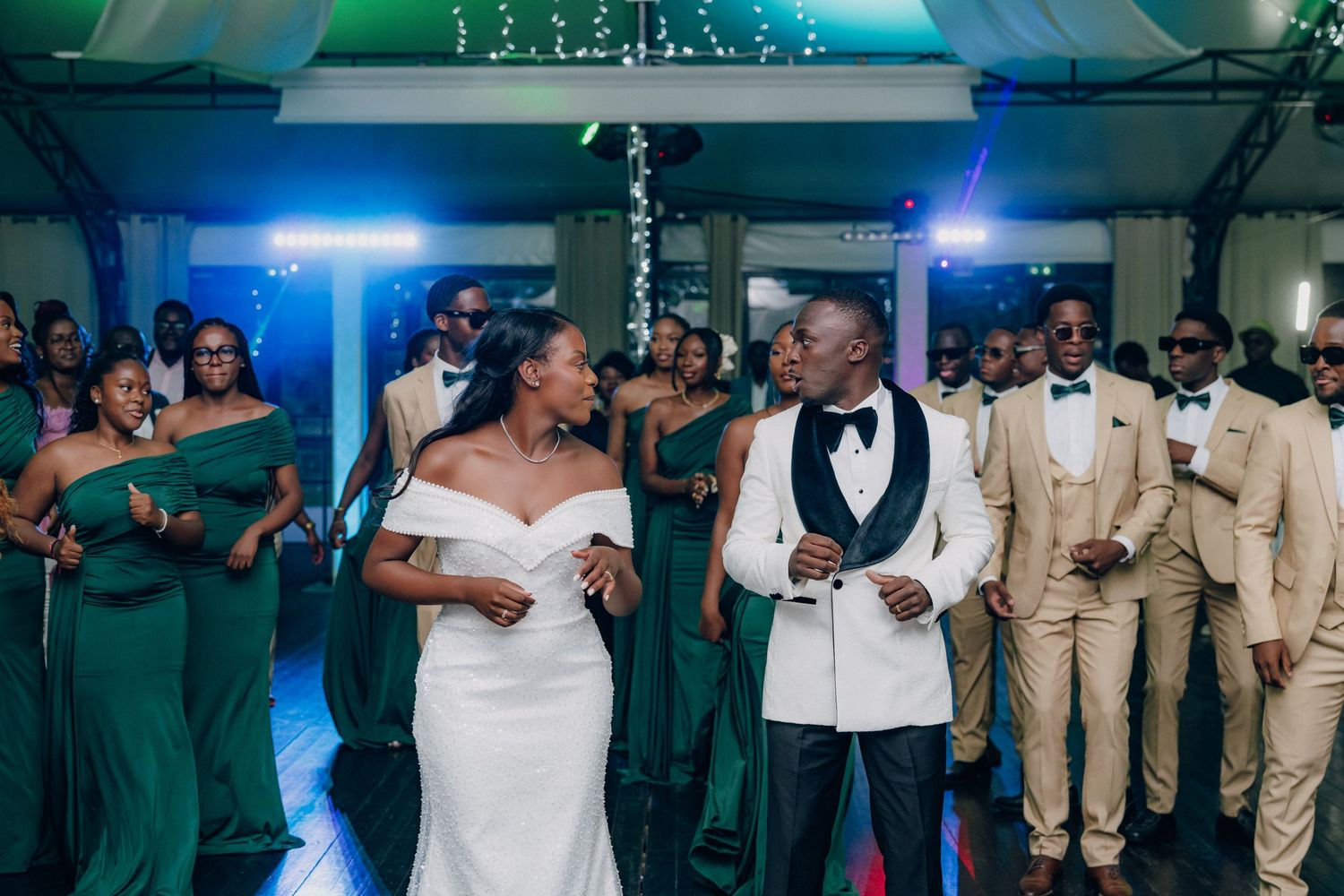 Wedding celebration with guests dancing under blue and green atmospheric lighting.