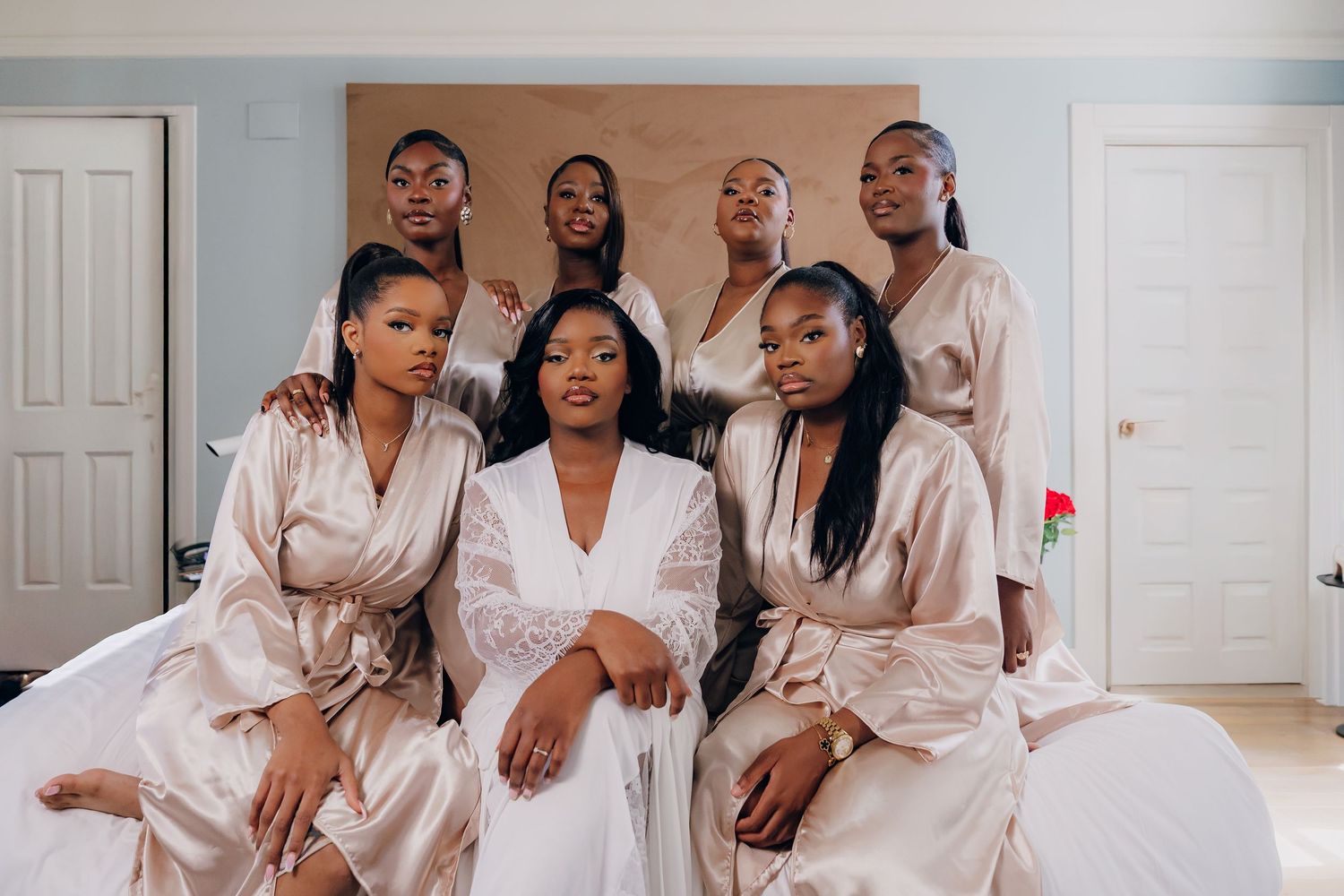 A group wearing matching silk robes poses together on a bed during pre-wedding preparations.