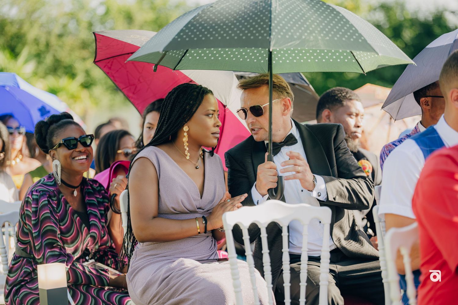 Wedding guests sitting under colorful umbrellas at an outdoor summer celebration.