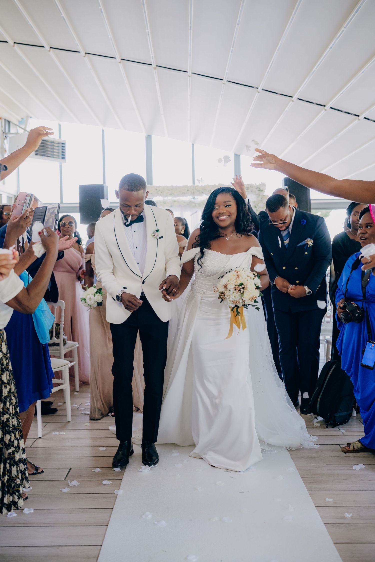 A joyous wedding celebration with guests cheering as newlyweds walk down the aisle together.
