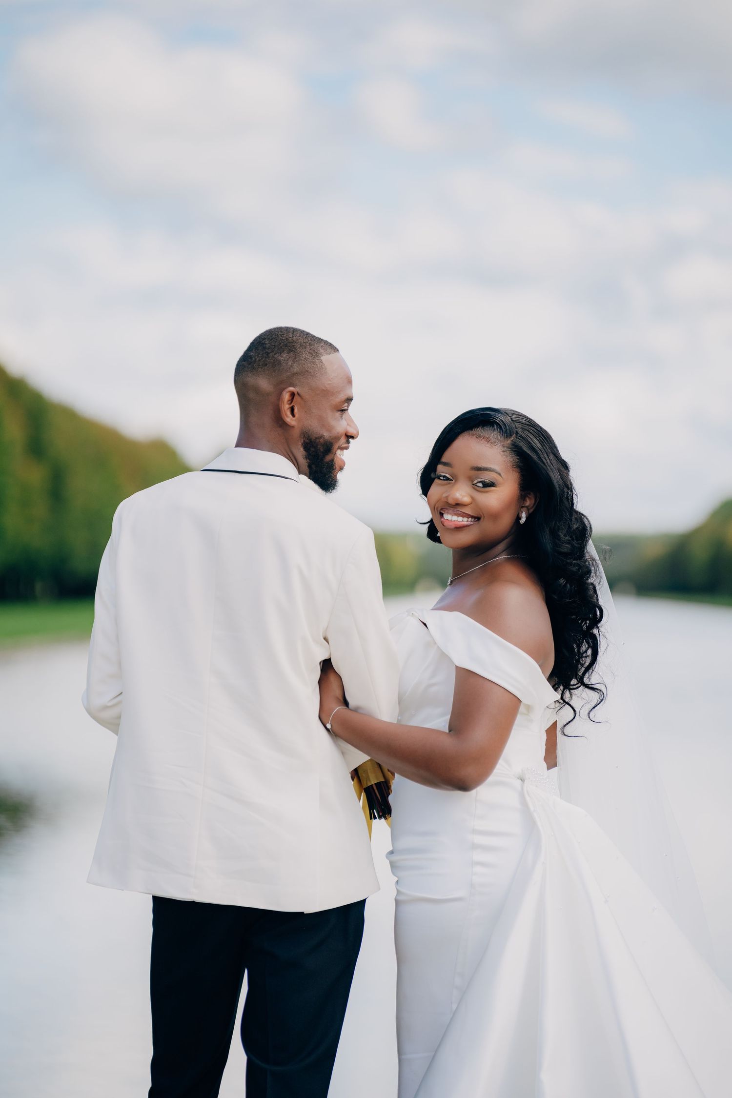 A romantic waterfront wedding photoshoot with the couple posing against a cloudy sky backdrop.