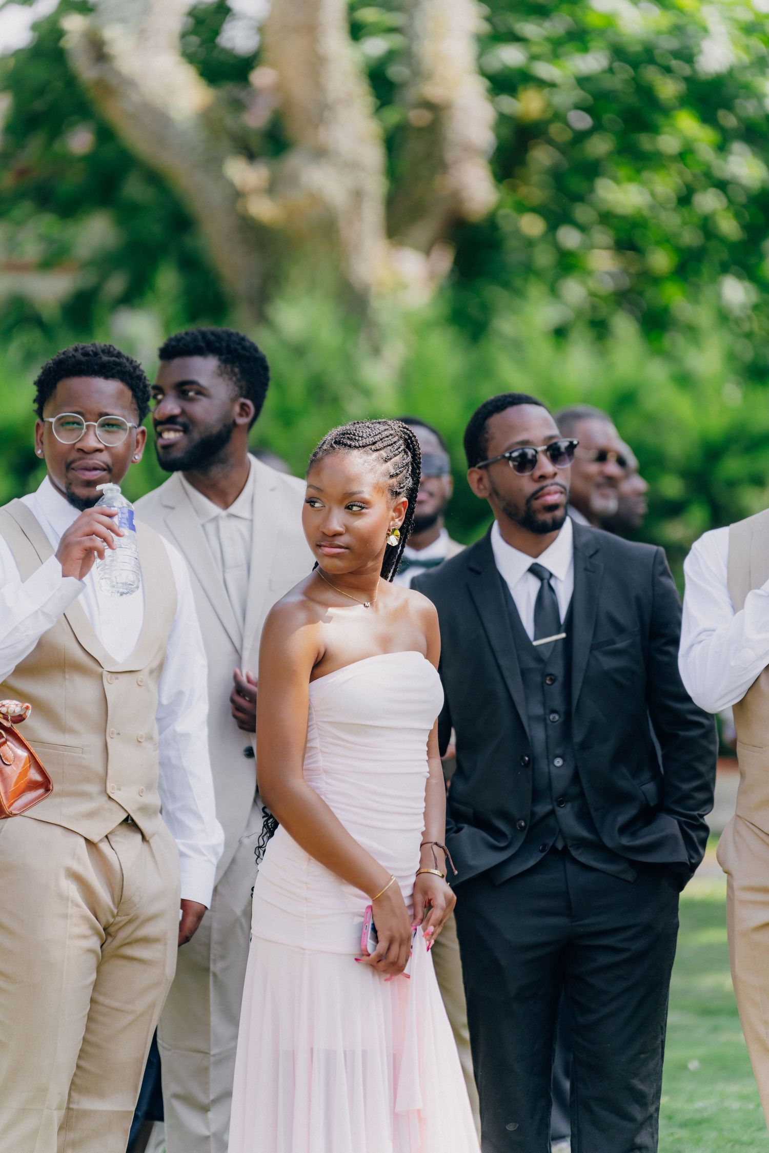 Wedding party members pose together in formal attire featuring beige suits and white dresses.