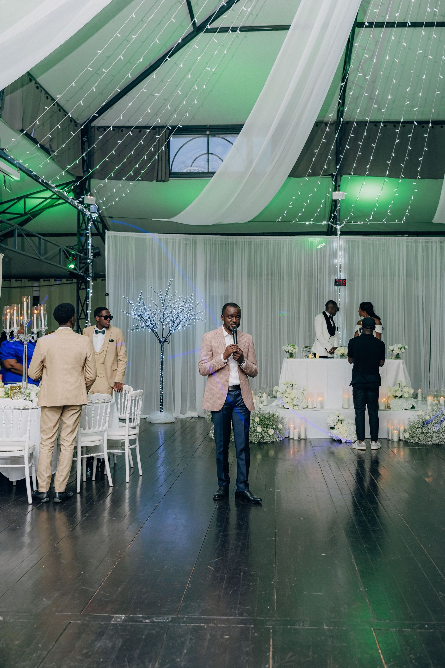 Modern event space with white curtains, green lighting and formal dining setup.