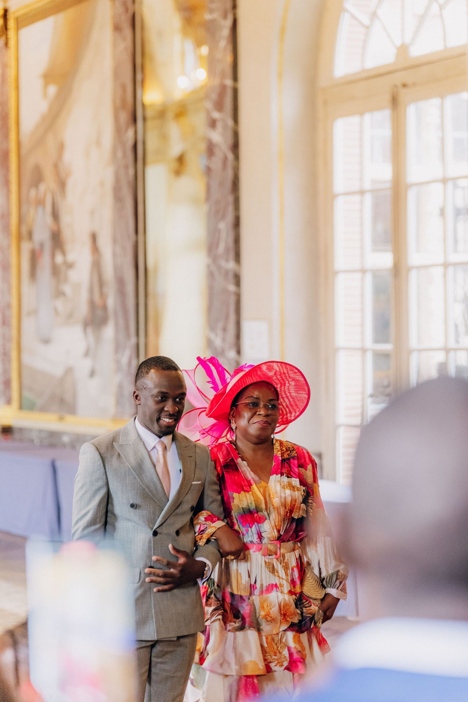 Wedding guests celebrate in an ornate palace hall with bright pink and colorful attire.