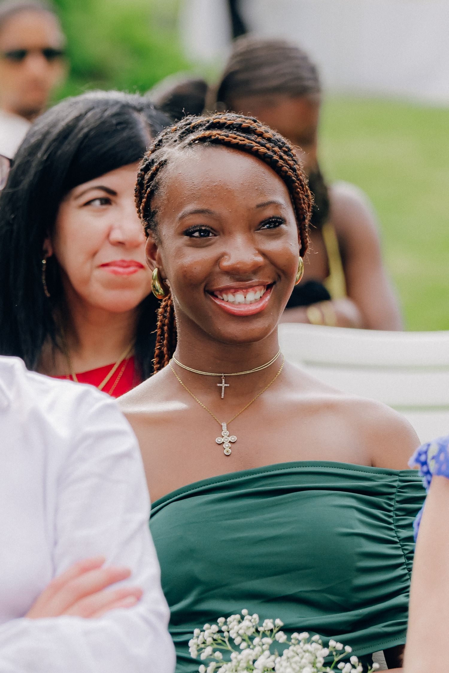 A bridesmaid in an elegant green dress smiles during an outdoor wedding celebration.