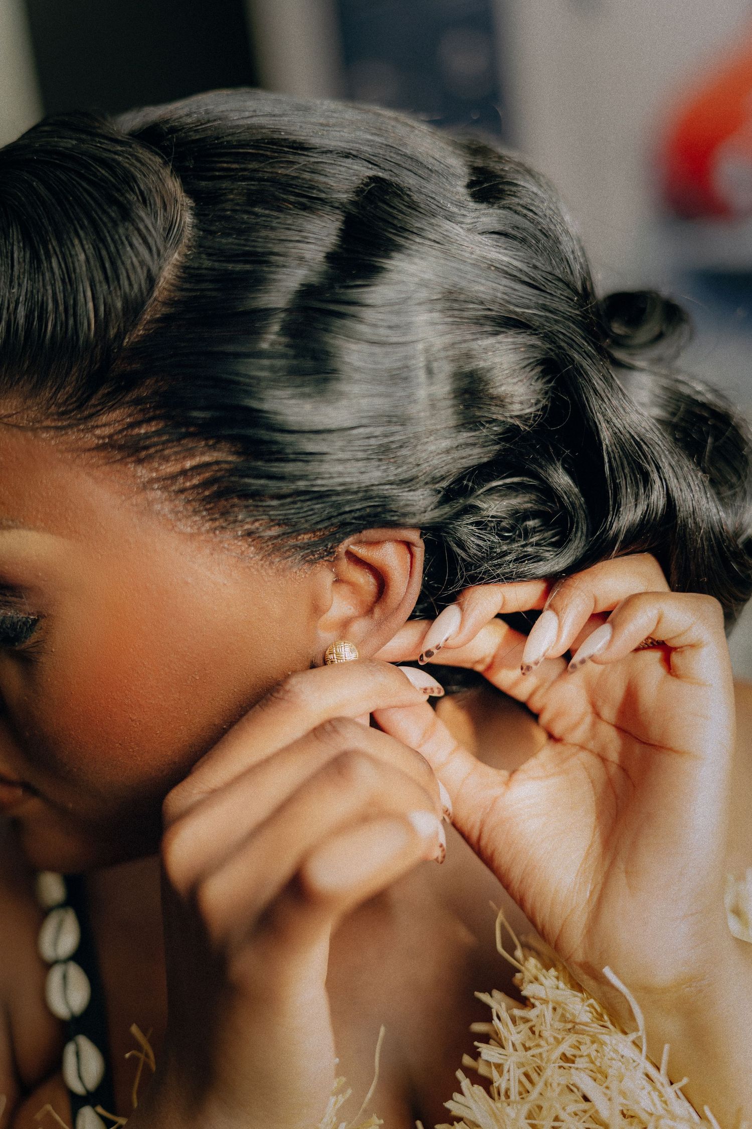 Close-up shot of someone putting in an earring with their dark hair styled in curls and adorned with seashell jewelry.