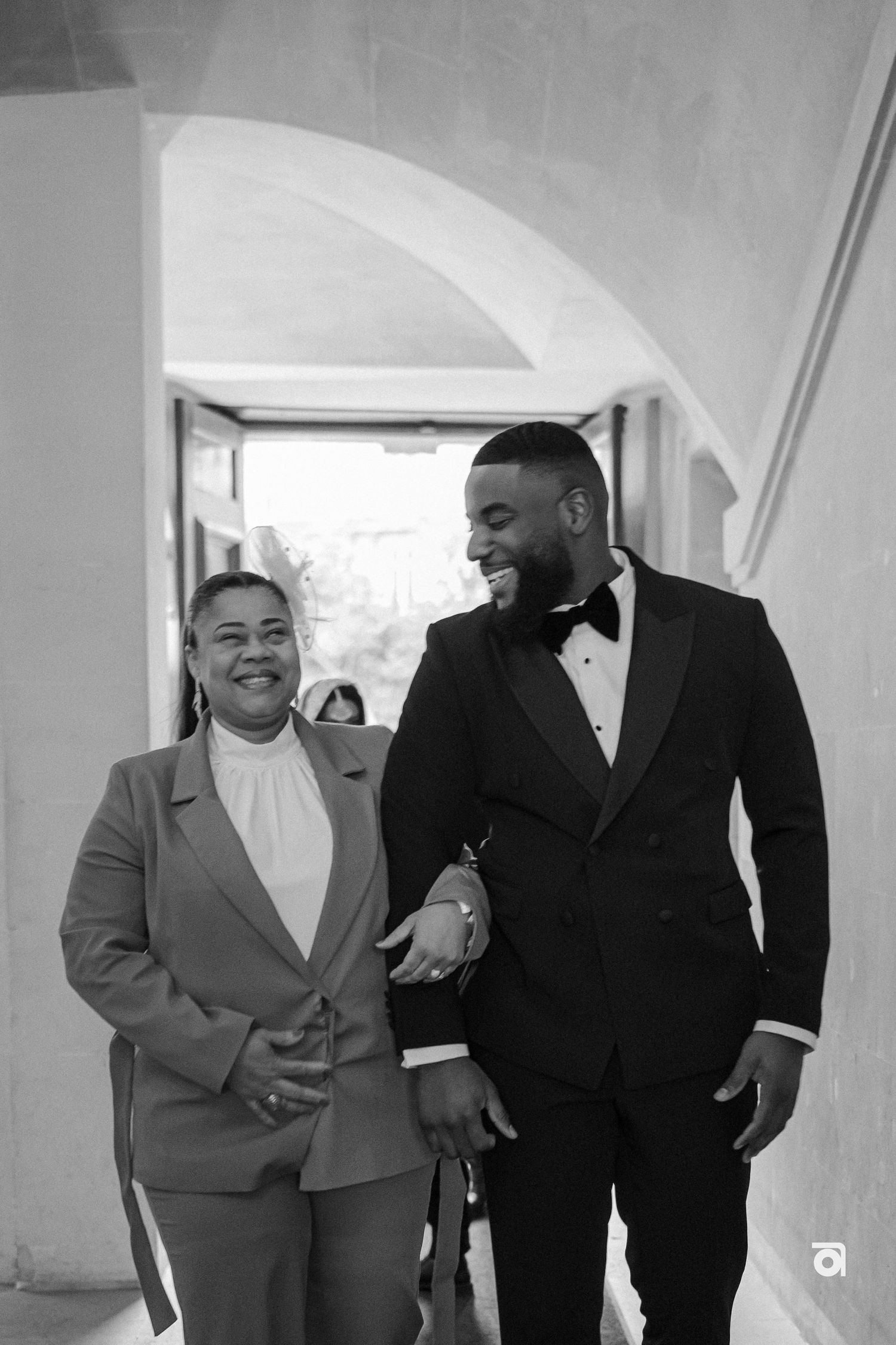 A joyful moment captured in black and white as bride and groom share laughter under an elegant archway.