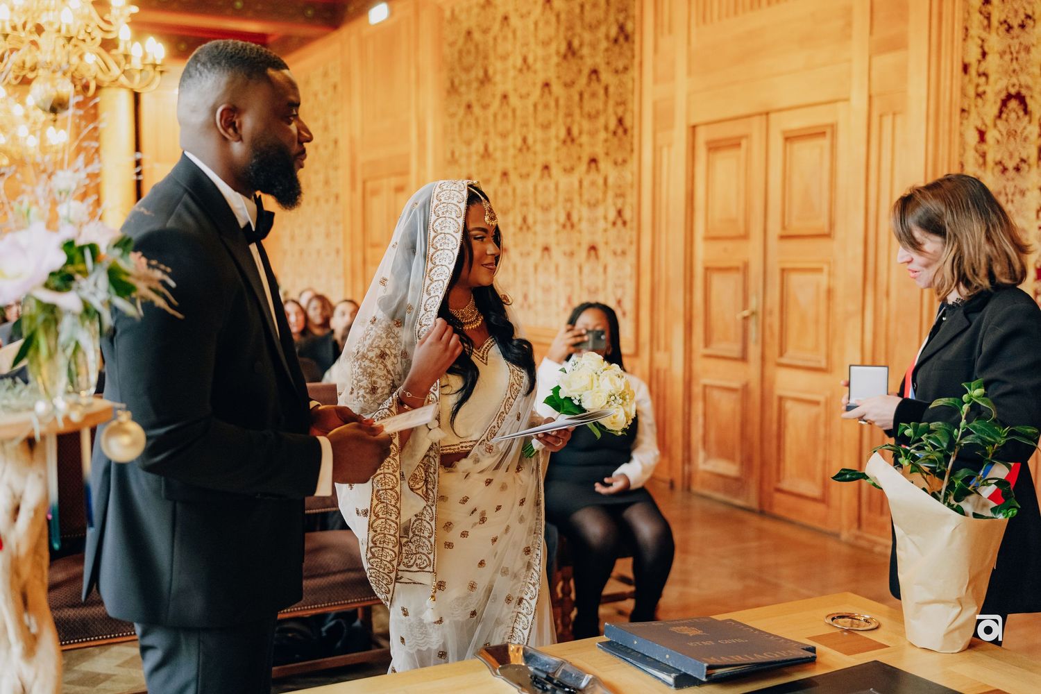 Wedding party gathered in an elegant room with gold wallpaper and ornate details during ceremony.