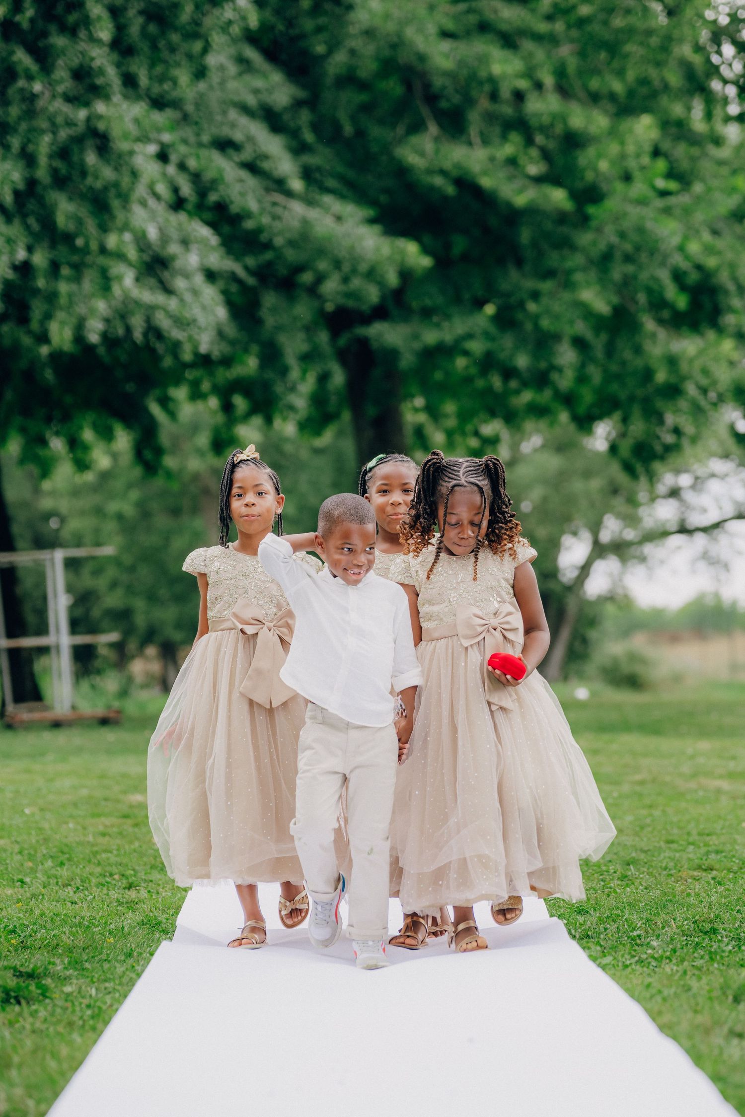 Young children in cream and white dresses pose together on white fabric outdoors.