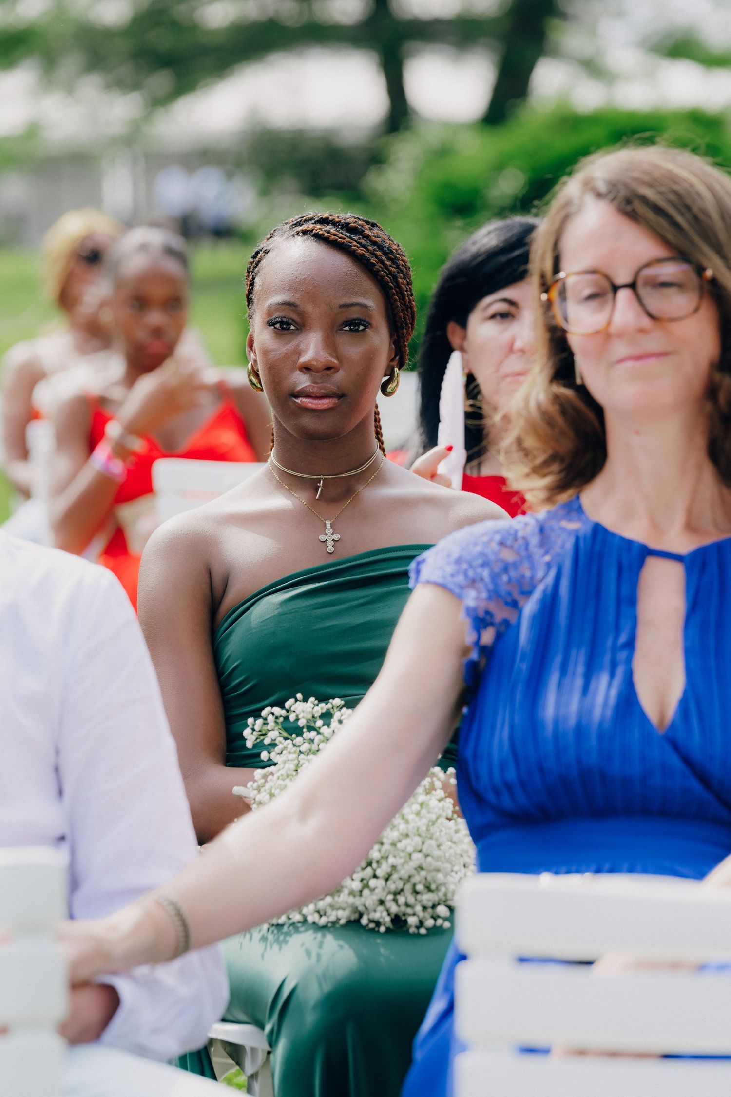 Wedding guests in formal attire seated at an outdoor ceremony with white chairs.