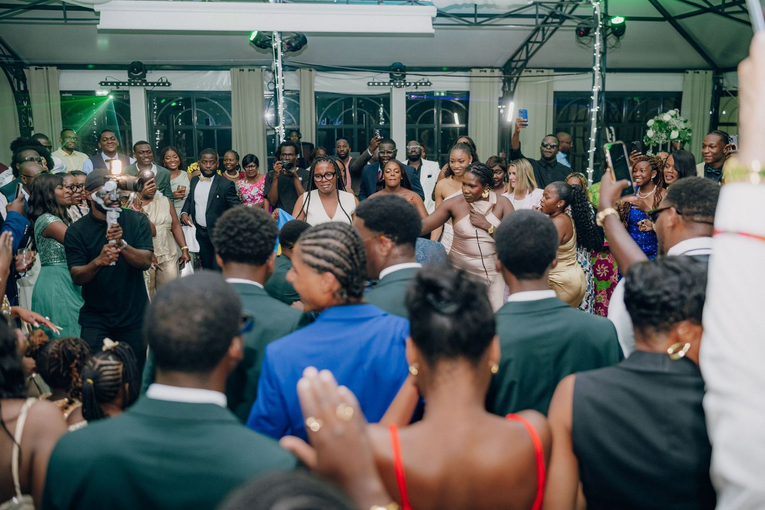 Wide view of wedding reception showing large crowd of guests gathered on dance floor.