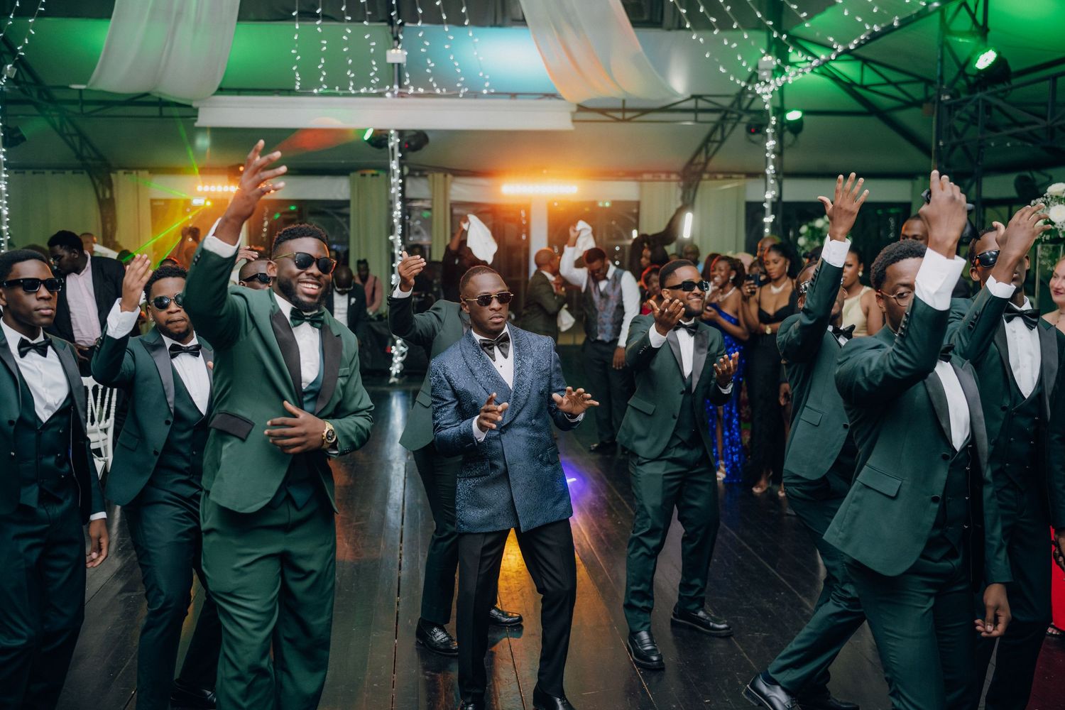 Wedding party members in formal attire dancing in formation under green ambient lighting.