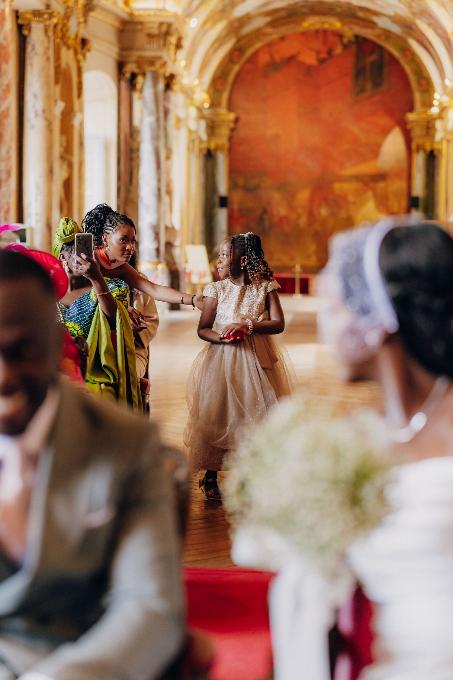 Guests celebrating in an ornate palace ballroom with elegant architecture and red carpet during a wedding ceremony.