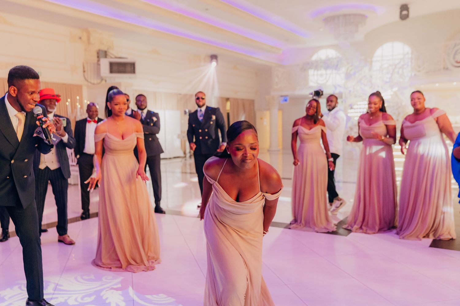 Wedding party dancing and celebrating in an elegant ballroom with pink and purple lighting.