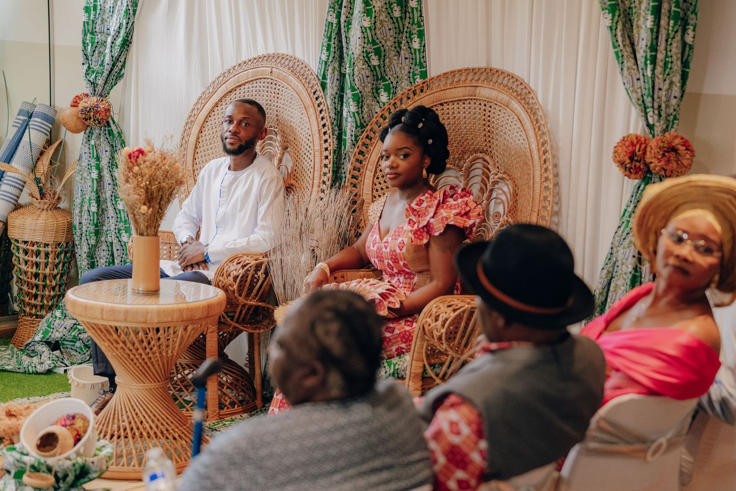 A traditional celebration gathering with guests seated around decorative furniture and floral arrangements.
