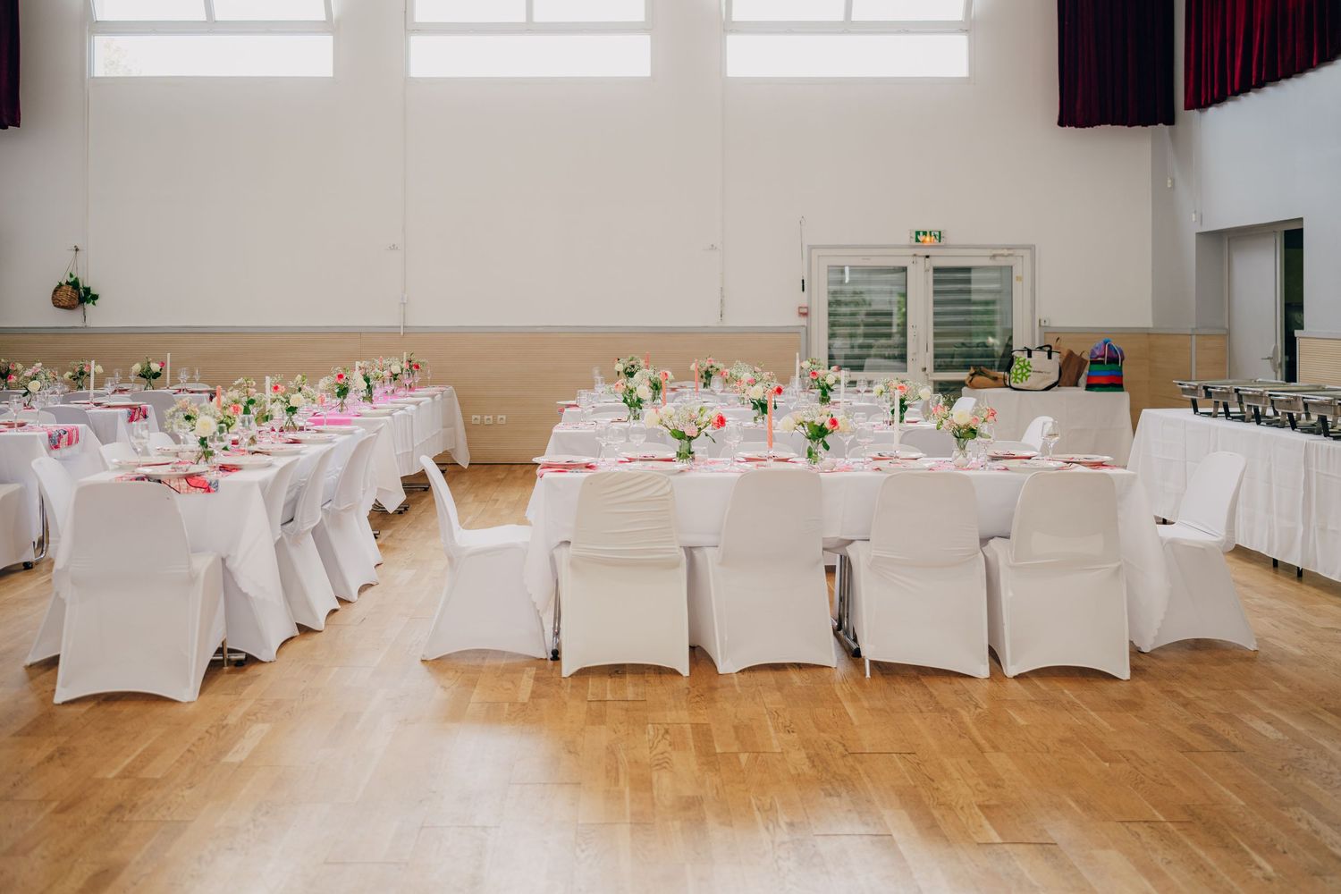 Wedding reception venue with elegant white-covered chairs and tables arranged in a spacious hall with wooden flooring.