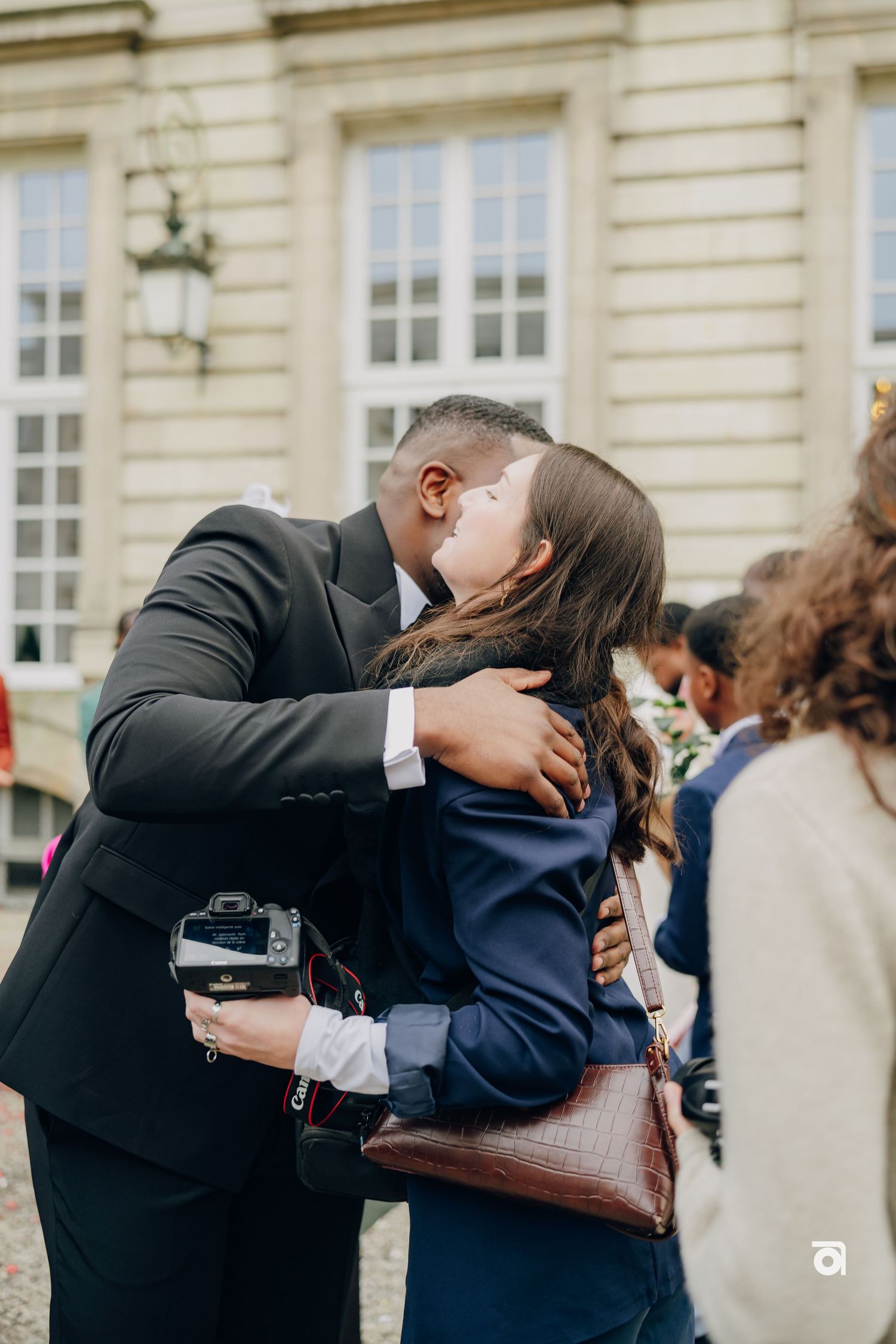 Two people share an intimate embrace outside a historic building during what appears to be a special occasion.