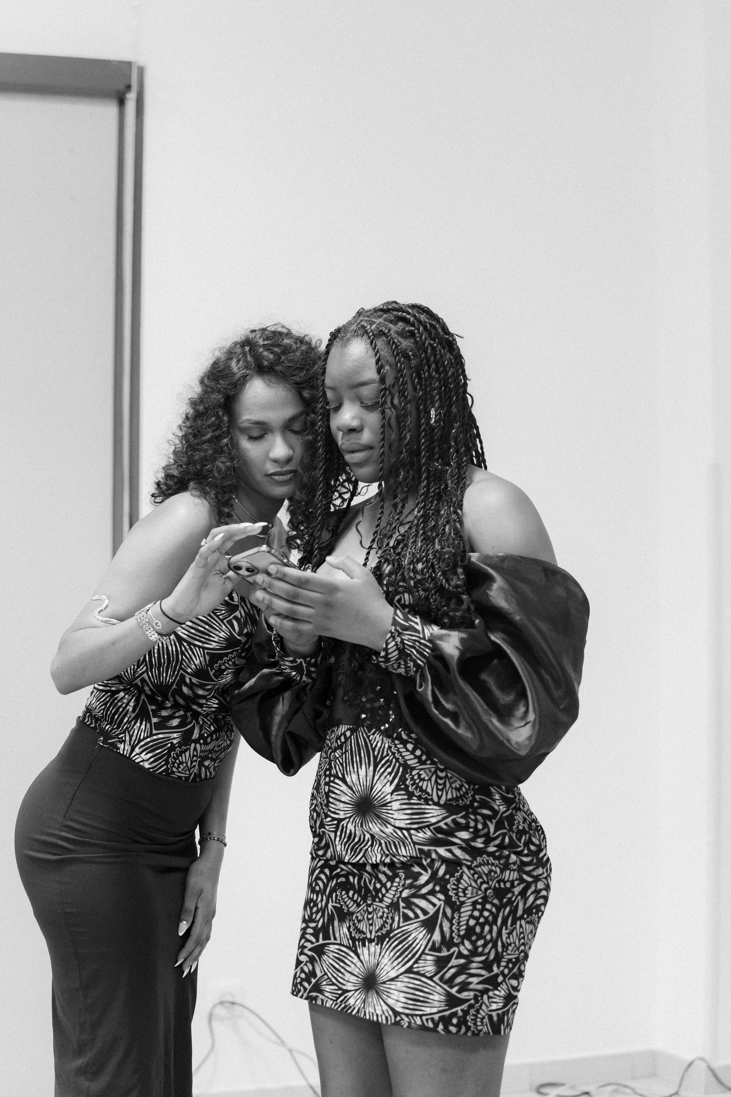 Two people in floral print outfits looking at a mobile device together in black and white photography.