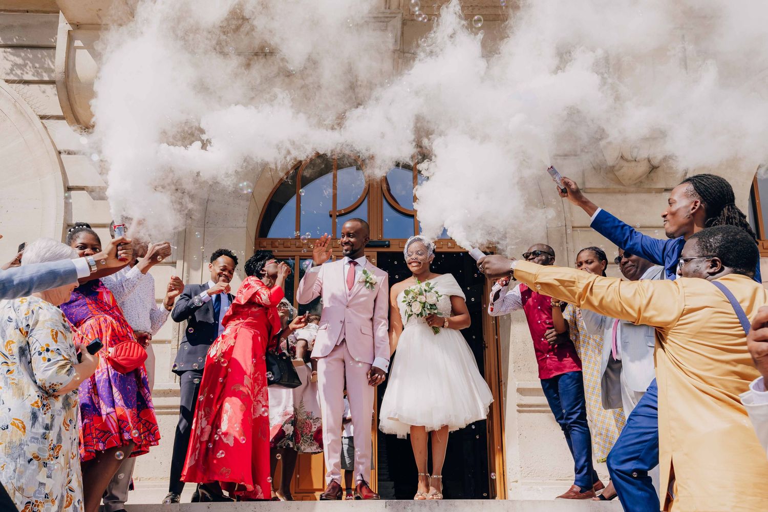 Wedding party celebrates with colorful smoke bombs creating dramatic effect during outdoor photo session.