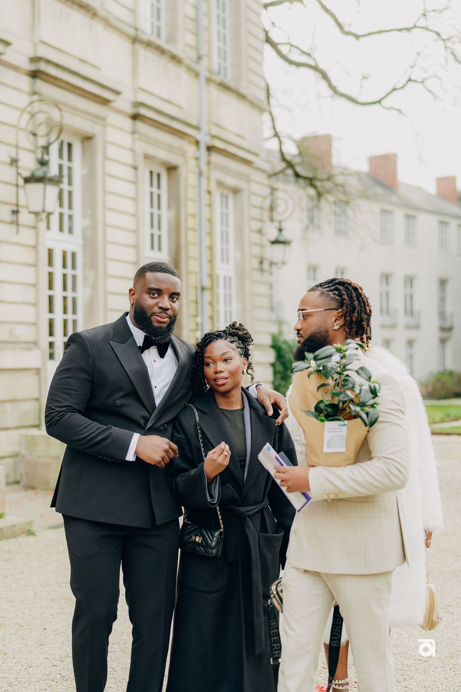 Three people in formal attire stand chatting outside historic building.