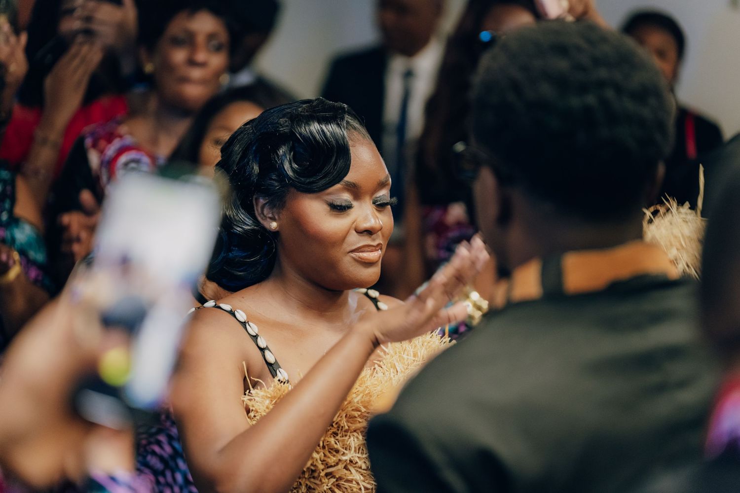 People dancing and celebrating at a festive event, with a person in a gold sequined dress in focus.