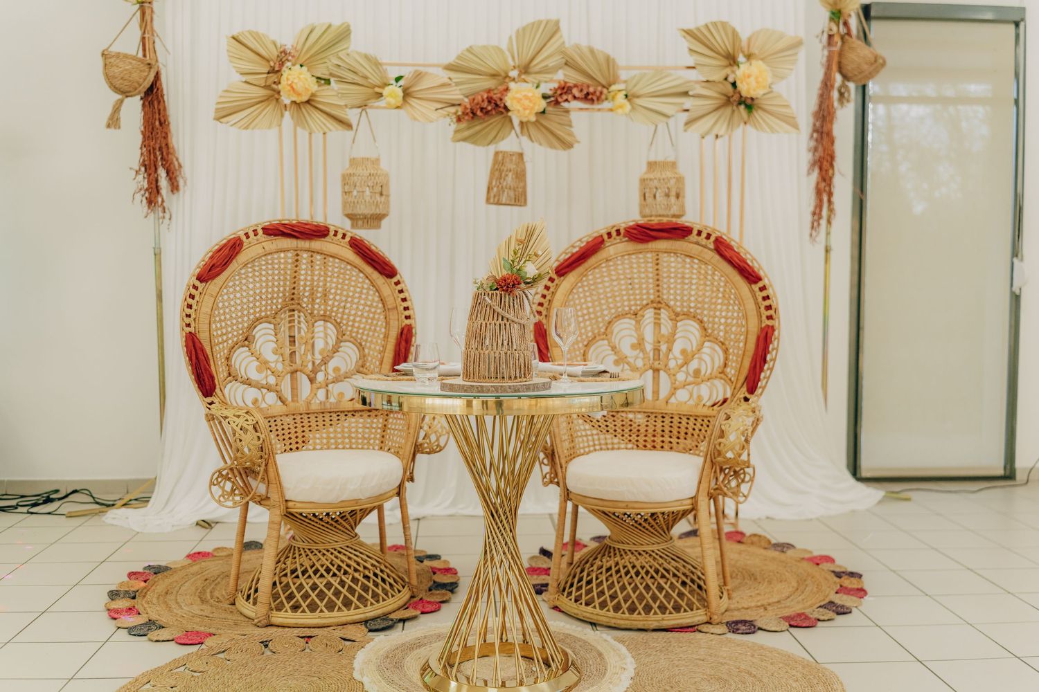 Vintage rattan peacock chairs with matching table decorated with gold bows in a romantic boho wedding setup.