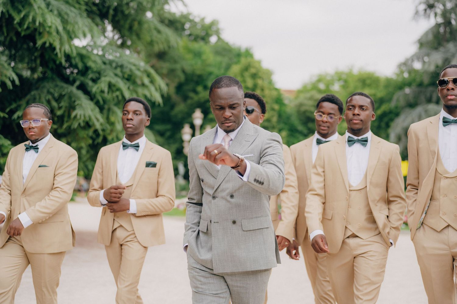 Groomsmen in tan and gray suits pose together during an outdoor wedding celebration.