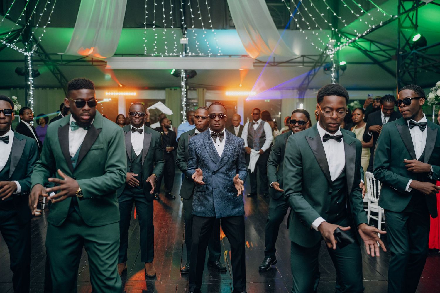 Groomsmen in dark suits lined up at wedding reception with dramatic lighting effects.
