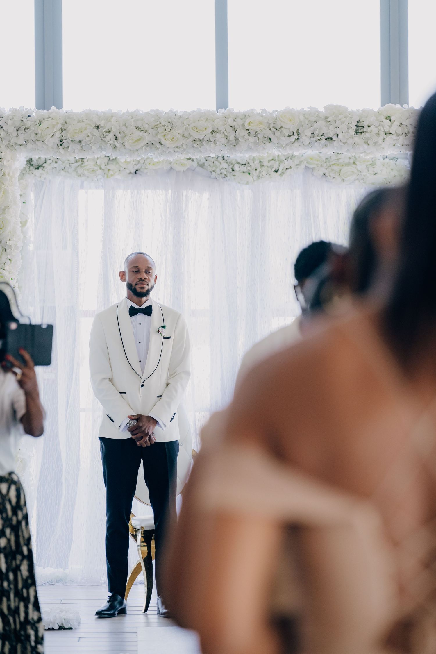 Wedding ceremony setup with white floral decor and sheer curtains in a modern indoor venue.