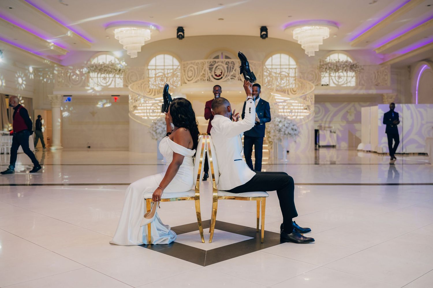 Wedding guests dance and mingle on an elegant ballroom dance floor illuminated by purple lighting.