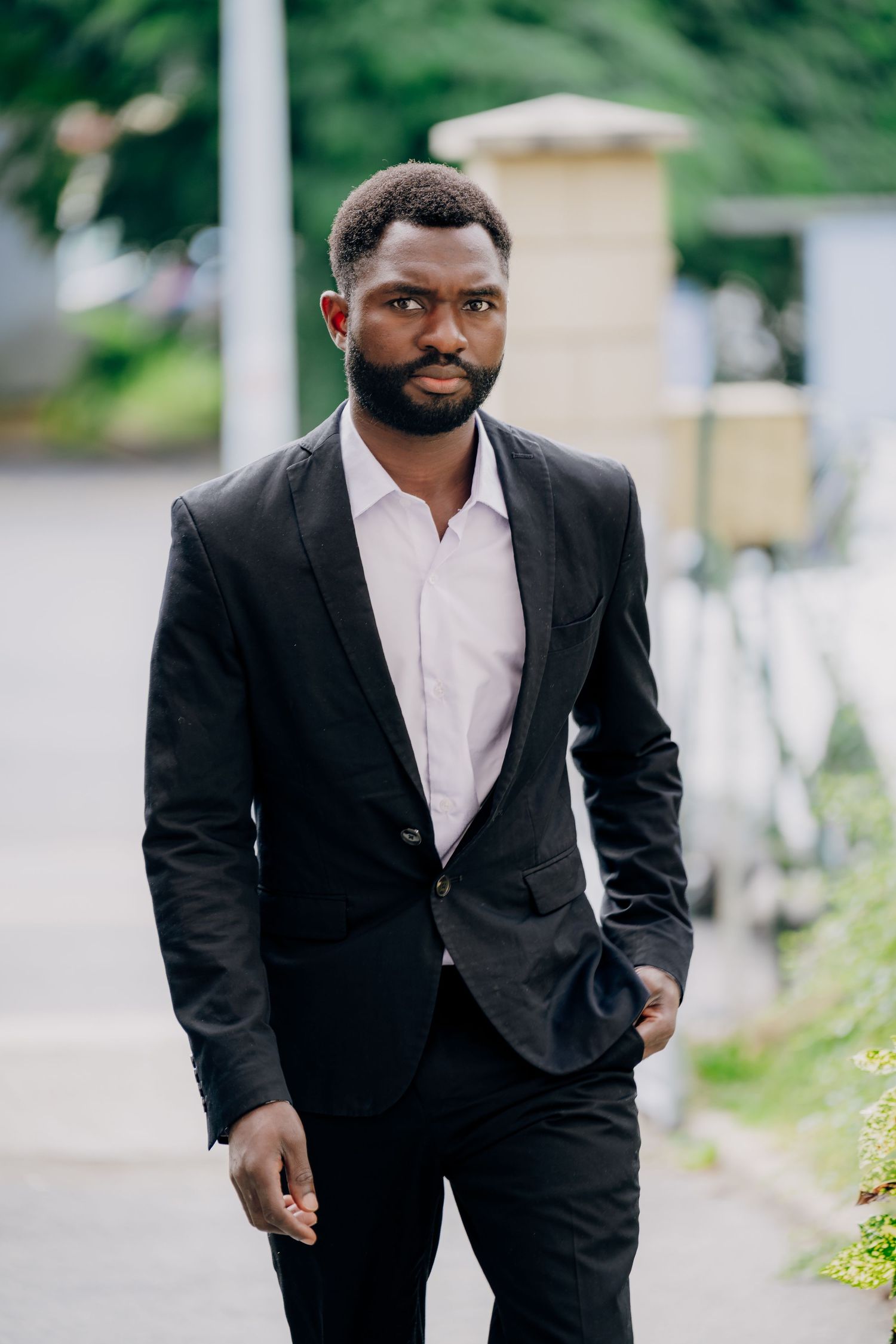 Professional wearing a black suit and white shirt walks purposefully down an outdoor path.