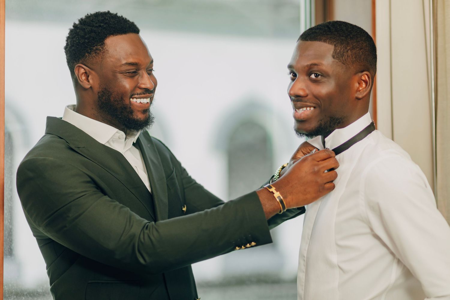 Two people sharing a joyful moment while adjusting formal attire.