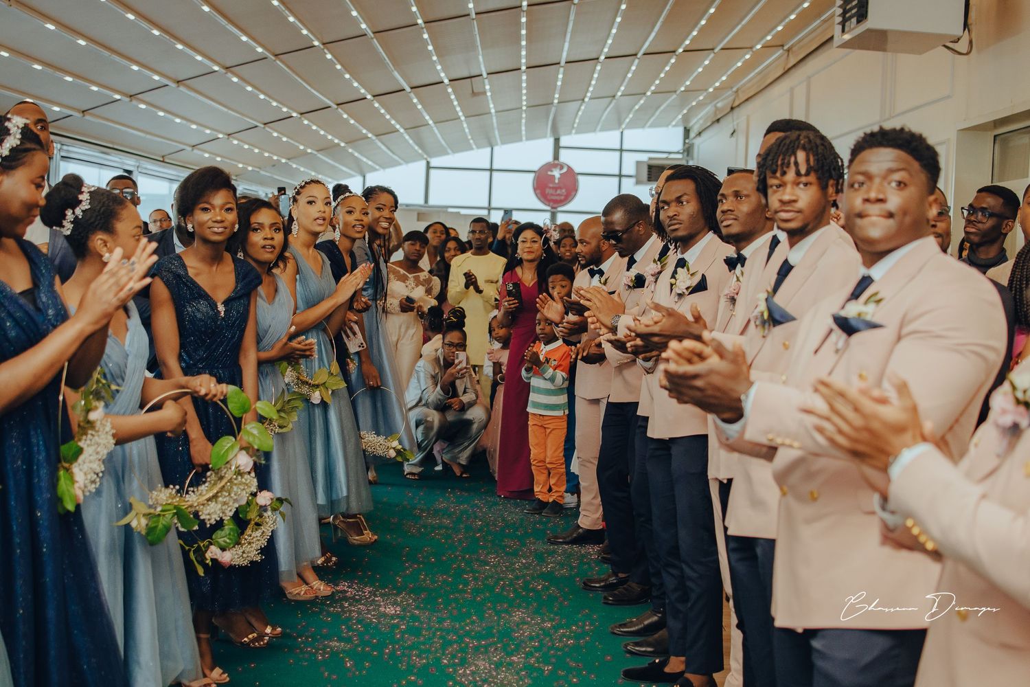 Wedding party in navy dresses and cream suits lined up in celebration at indoor venue.