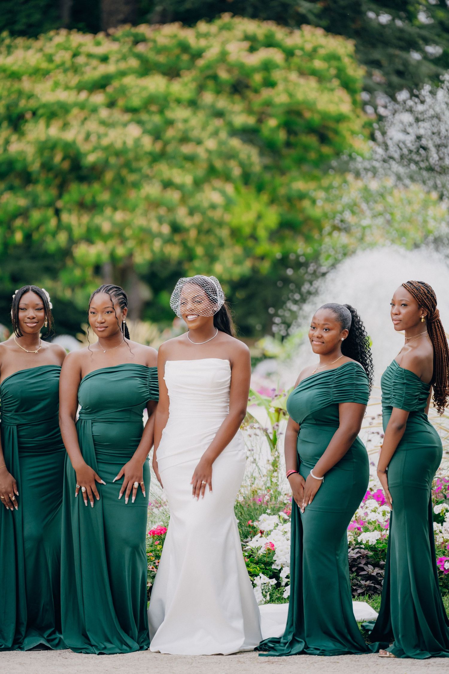 Wedding party in emerald green dresses posed in a garden setting with the bride in white.