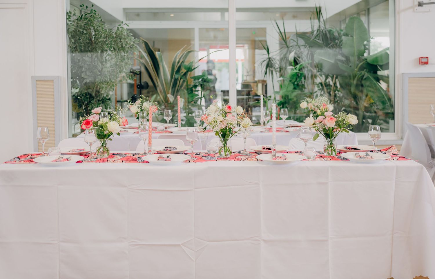 A panoramic view of an elegant wedding reception venue decorated in pink and white with tropical greenery accents.
