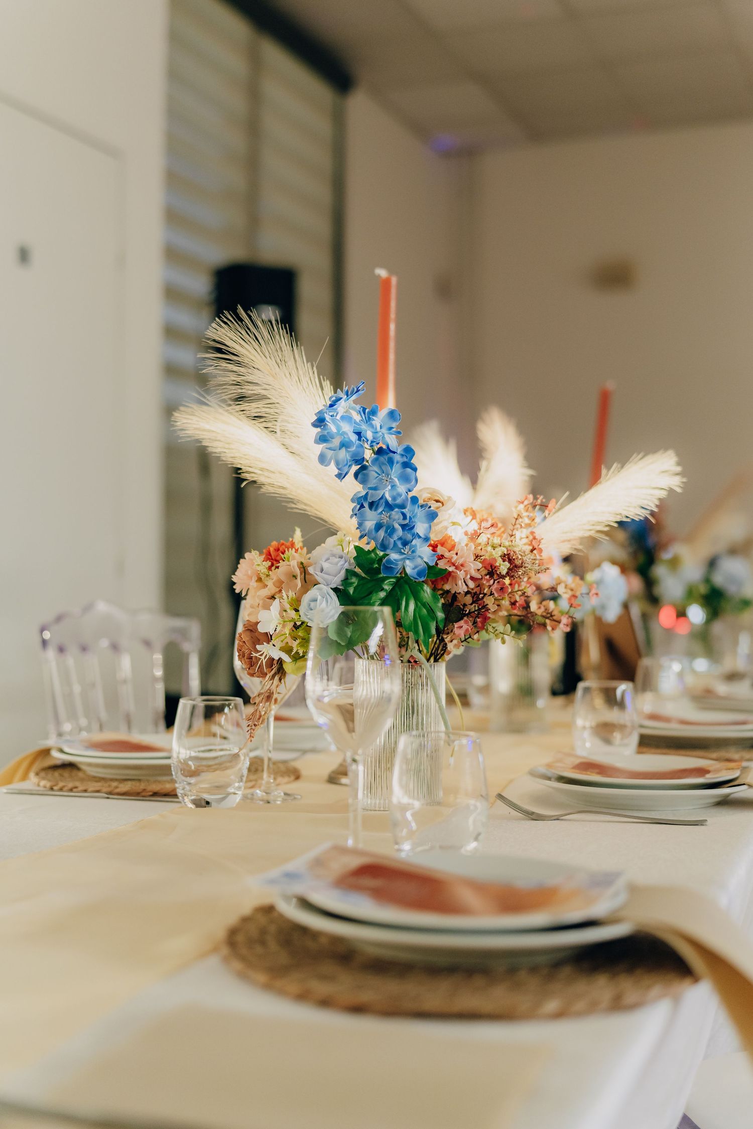 Elegant table setting with blue hydrangeas and dried flowers in glass vases on white tablecloth with woven placemats.