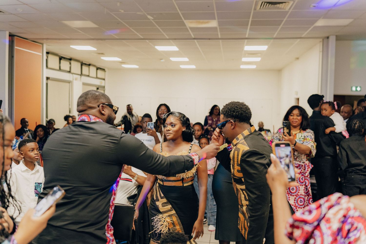 A crowded room of people celebrating and dancing together at an indoor event with bright lights.