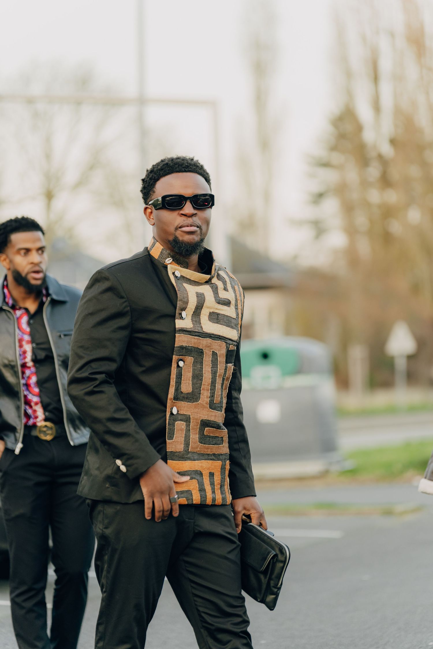Stylish man wearing sunglasses and geometric print jacket walks confidently outdoors.