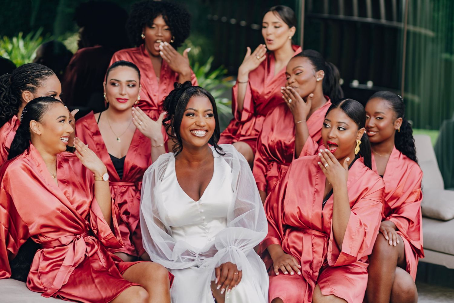 Wedding party in matching pink satin robes gathered around someone in white.