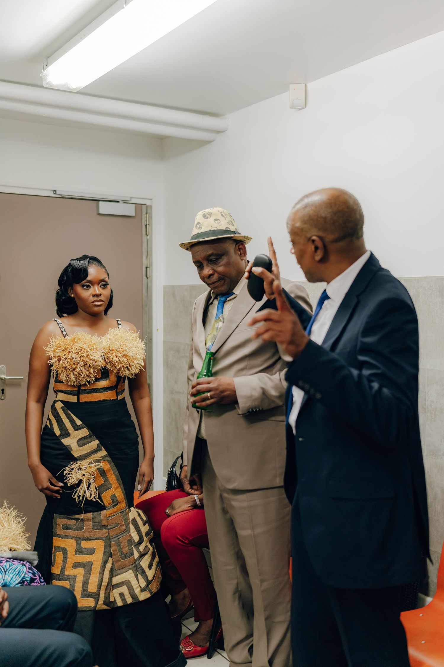 A group stands in a white room, with someone wearing a stunning black and gold patterned dress with feather details.