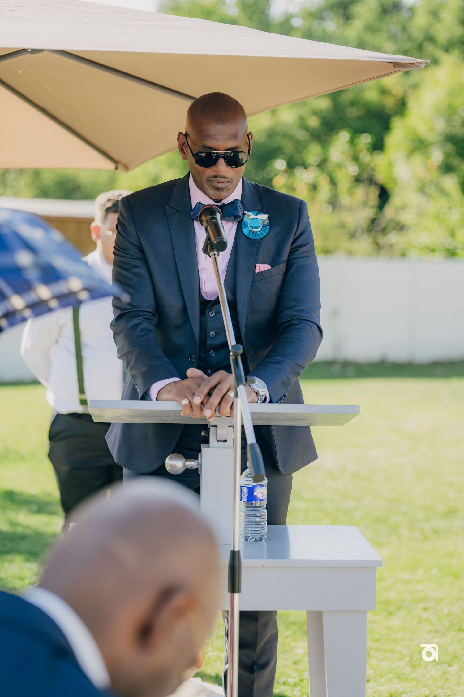 A DJ performs at an outdoor wedding reception behind professional equipment under a beige umbrella.