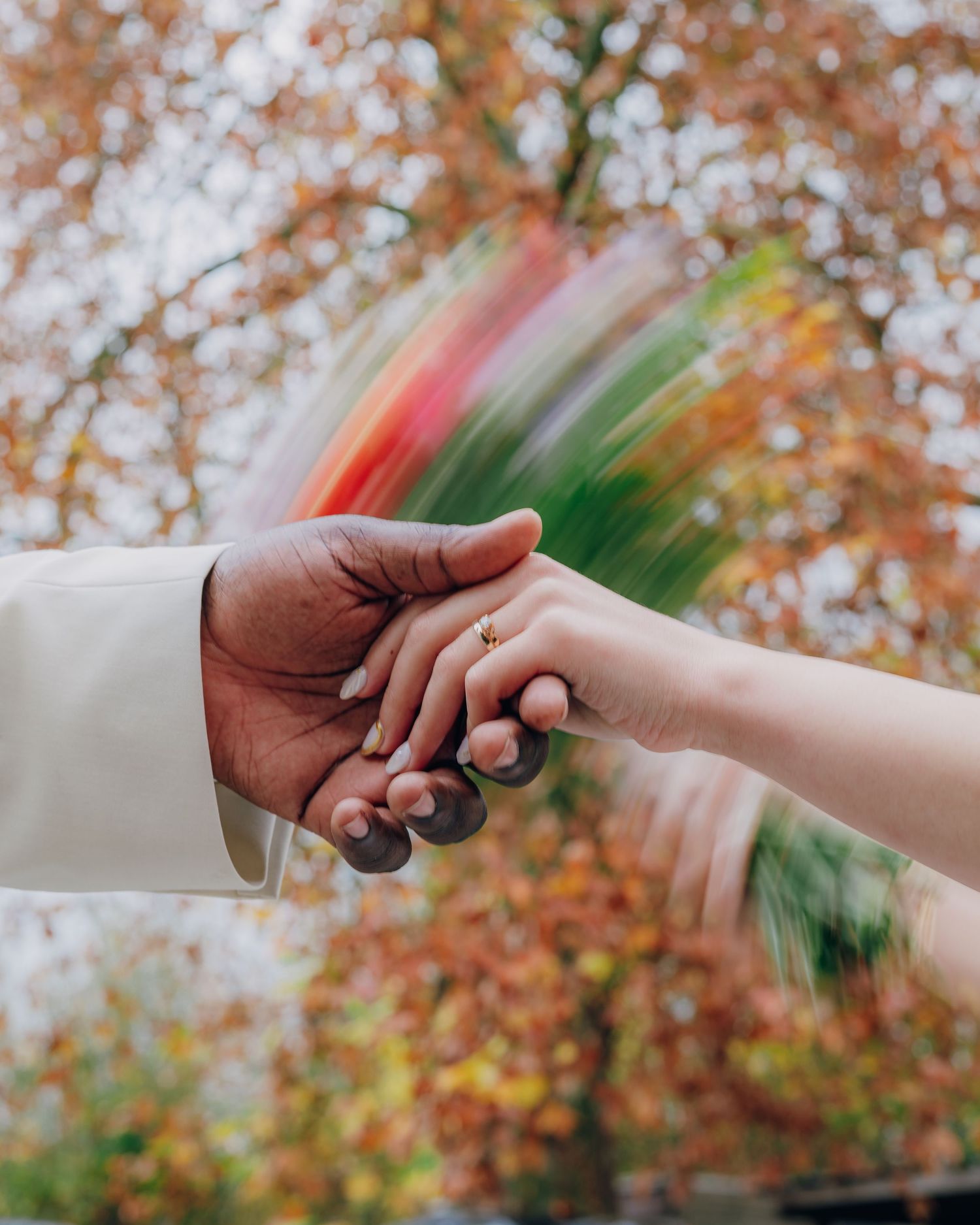 Two hands from different people reaching out to connect against a blurred autumn background with orange foliage.